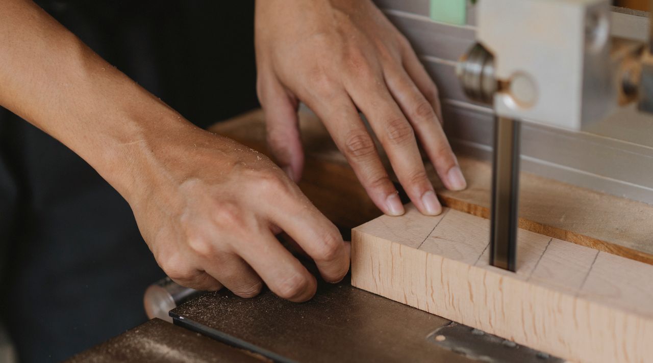 Crop unrecognizable joiner sawing lumber using band saw with metal blade while standing at table in workshop